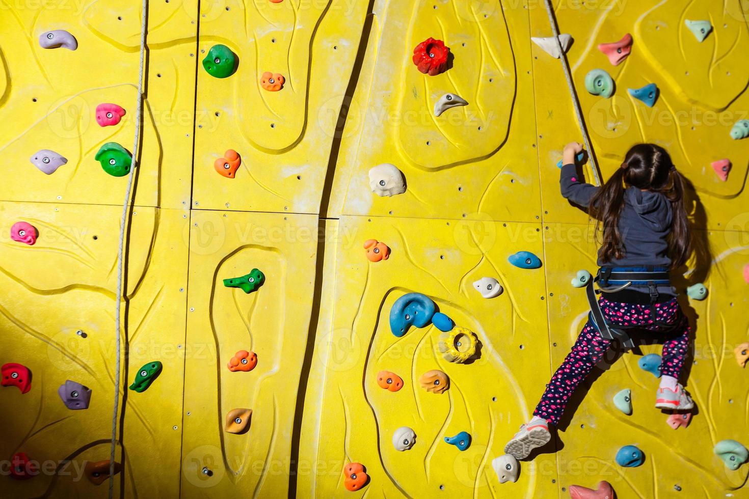 little girl climbing a rock wall indoor. photo