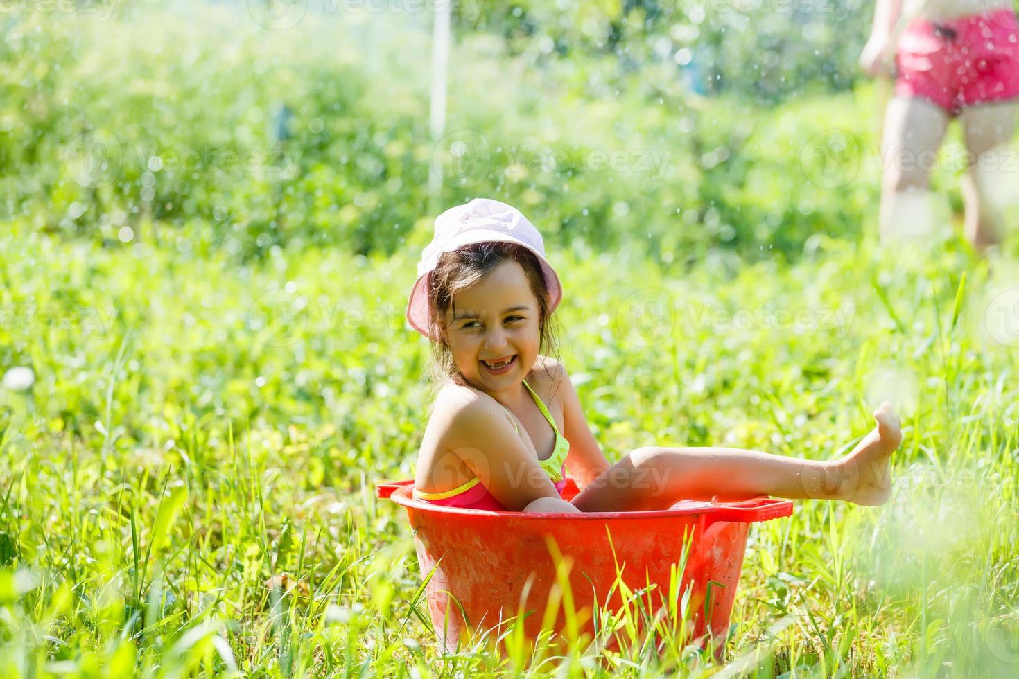 Child development in harmony with nature. Little beautiful girl playing fun with water and taking bath outdoors on the grass in vintage washing up bowl hygiene, happy childhood, nature concept photo