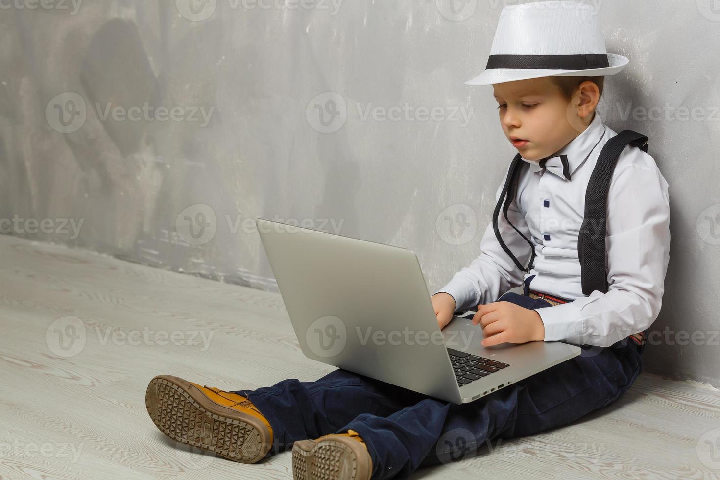 Little boy using laptop against grey wall background photo