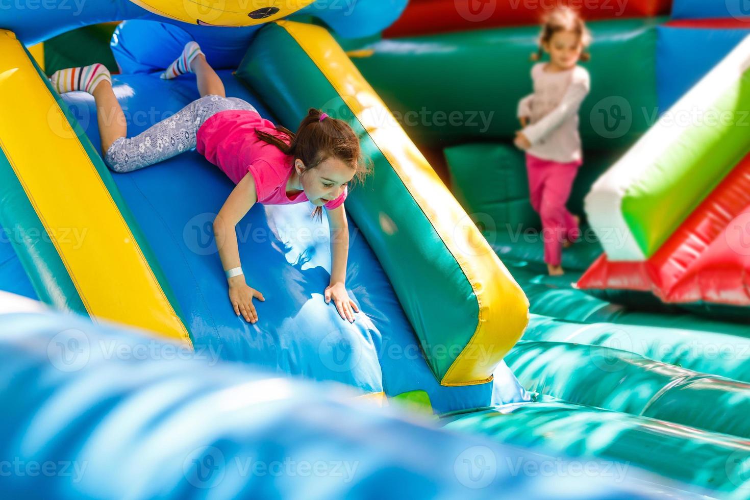 Child jumping on colorful playground trampoline. Kids jump in inflatable bounce castle on kindergarten birthday party Activity and play center for young child. Little girl playing outdoors in summer photo