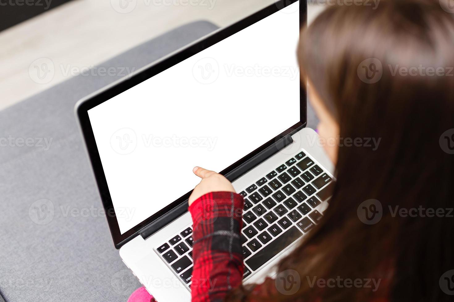 The little girl sits at a table with surprise looks at the laptop. photo