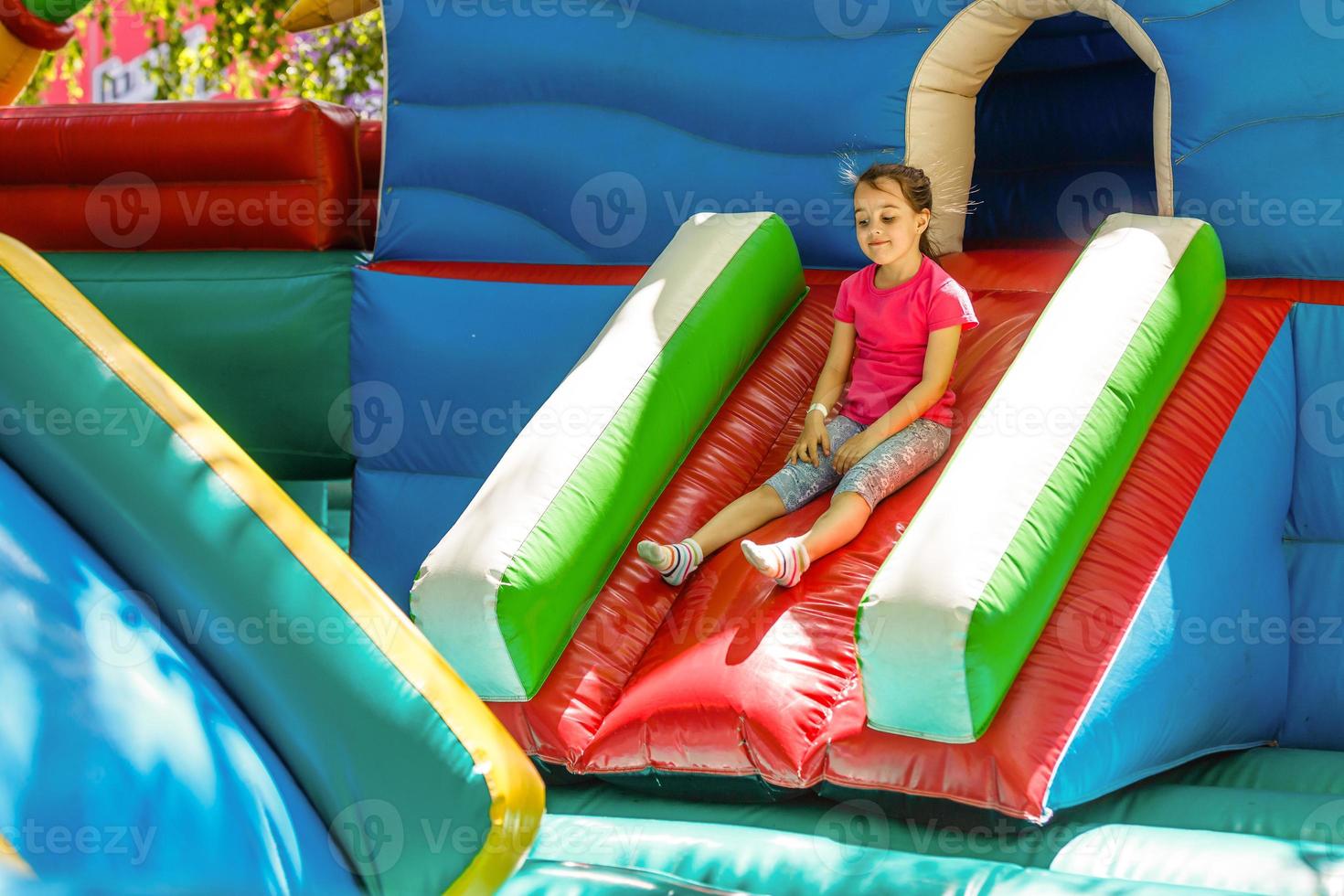 Happy little girl having lots of fun on a jumping castle during sliding. photo