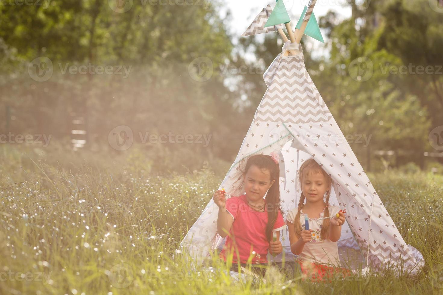 Two happy laughing little girls in camping tent in dandelion field photo