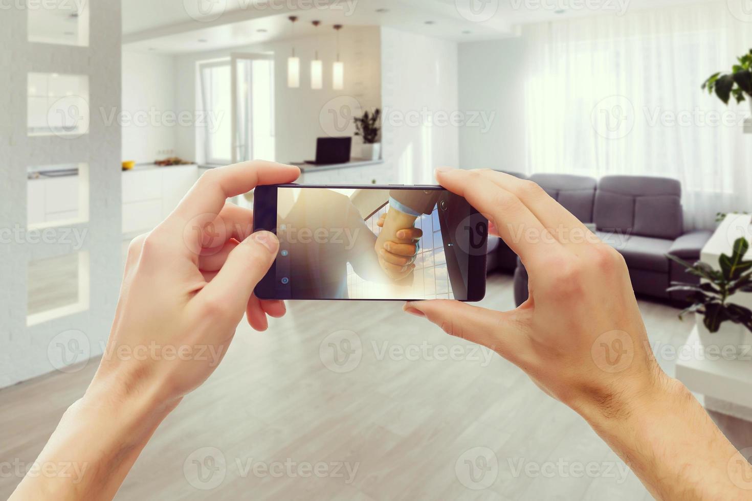 dos manos sosteniendo un teléfono inteligente móvil y tomando una foto en una moderna sala de estar y cocina de lujo