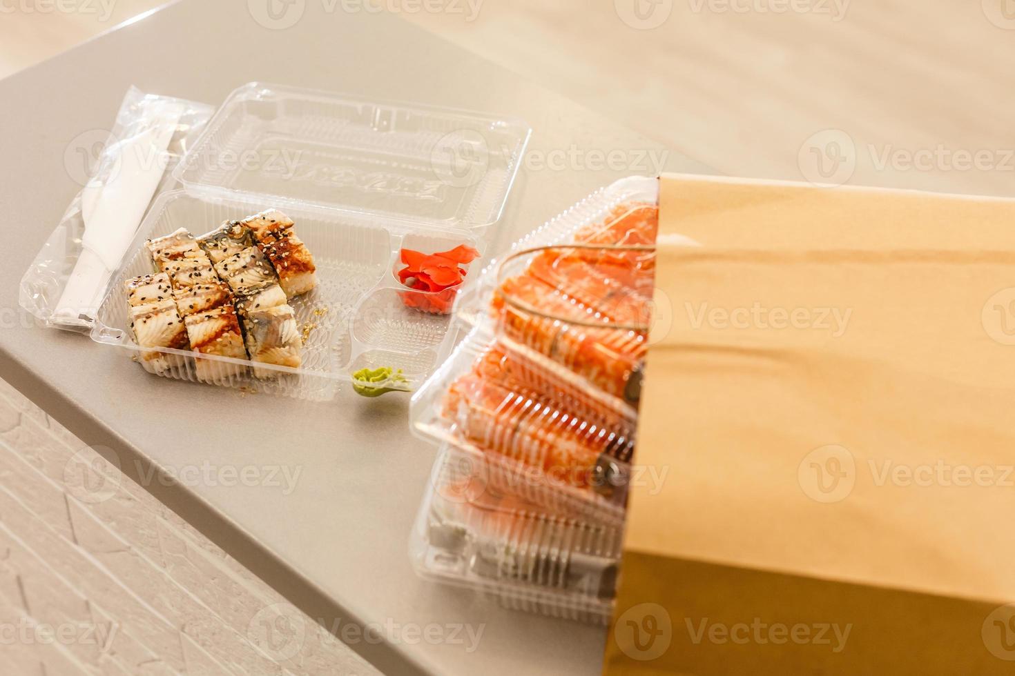 Sushi rolls in plastic box near paper package on white table. Delivery. Take away. photo