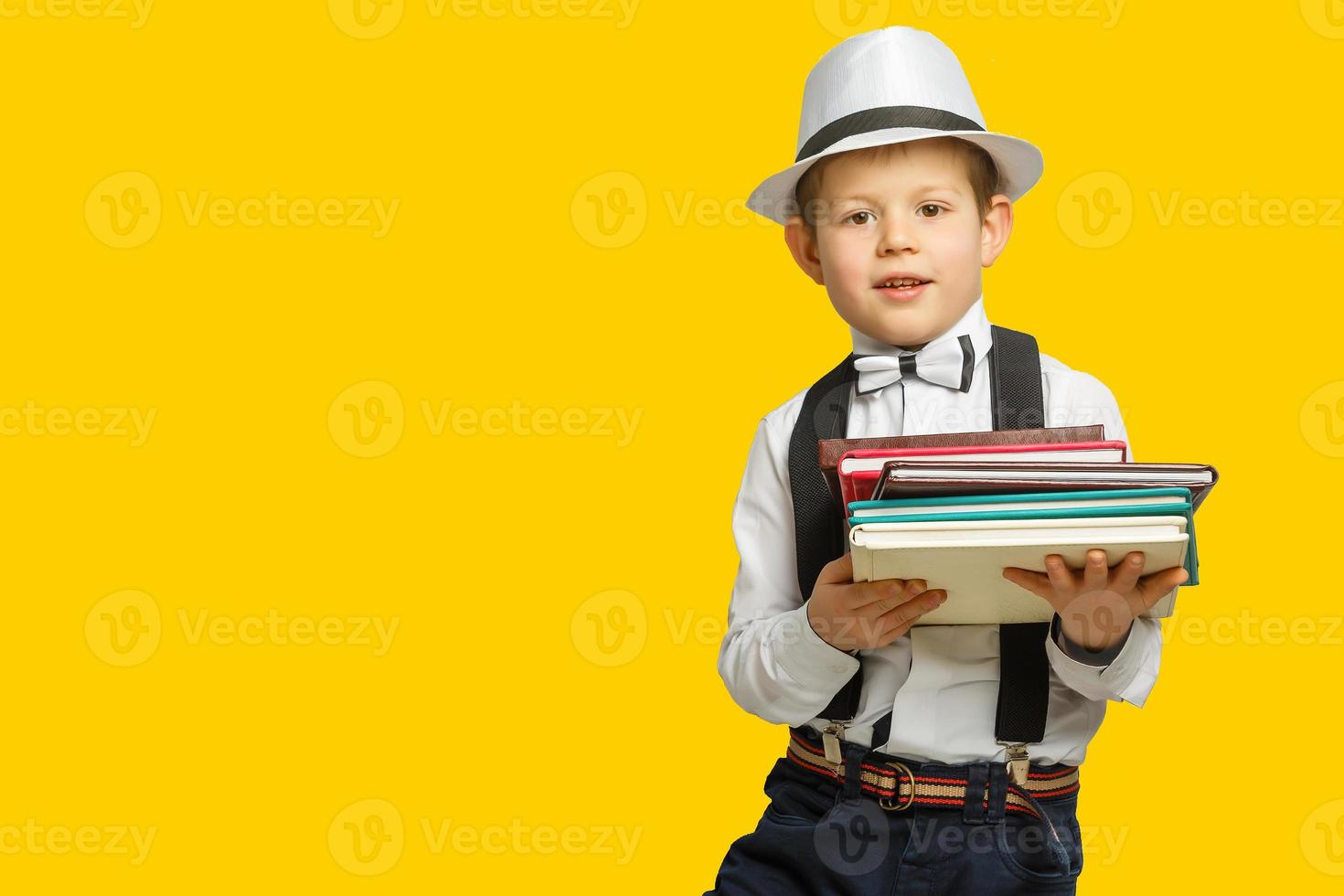 Happy smiling boy in glasses with thumb up is going to school for the first time. Child with school bag and book. Kid indoors of the class room with blackboard on a background. Back to school. photo