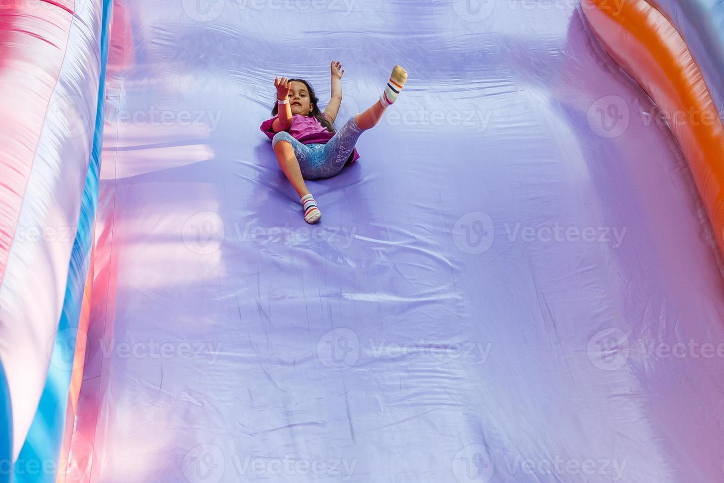 Happy little girl having lots of fun on a jumping castle during sliding. photo