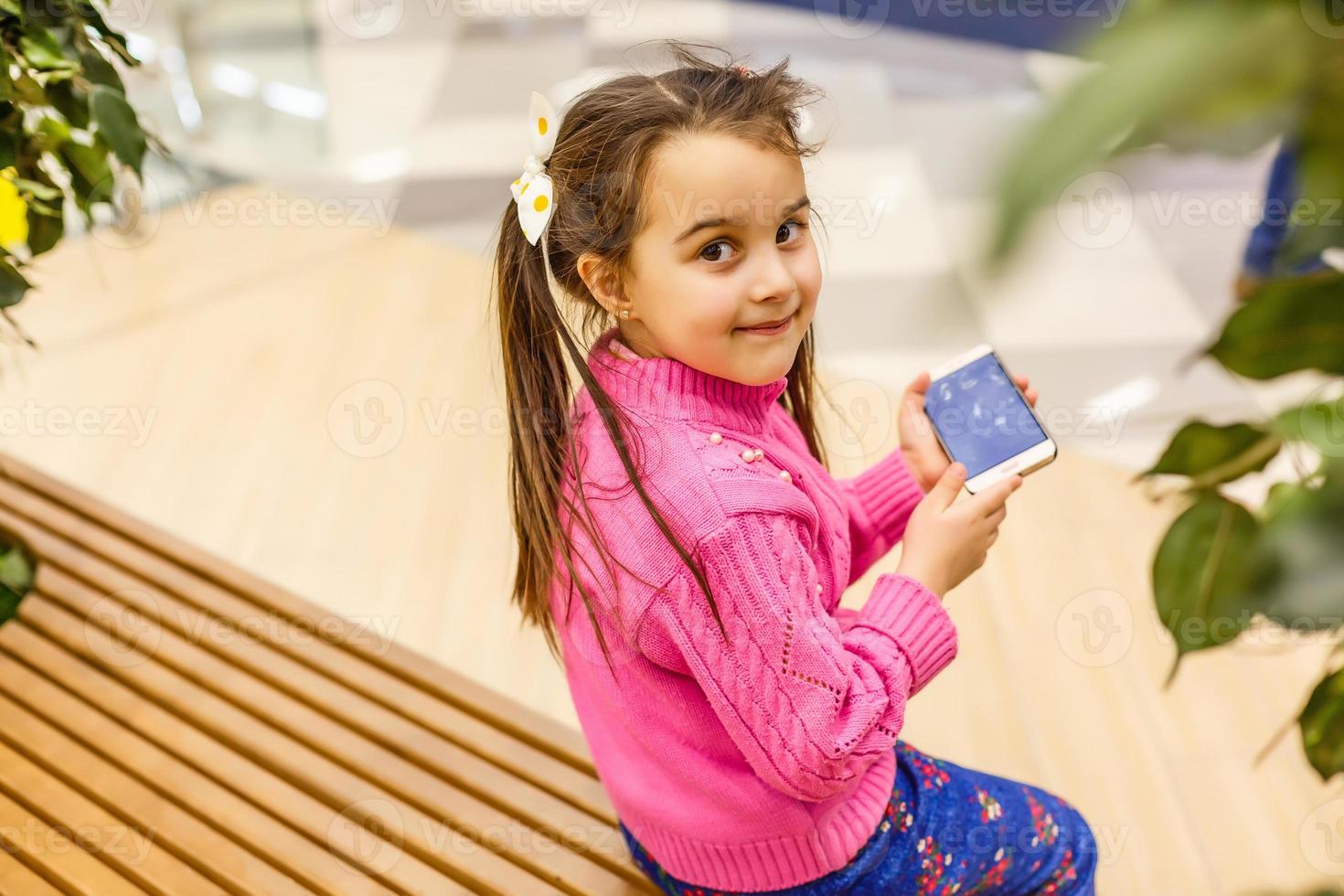 niña en rosa habla por teléfono móvil y en el centro comercial foto