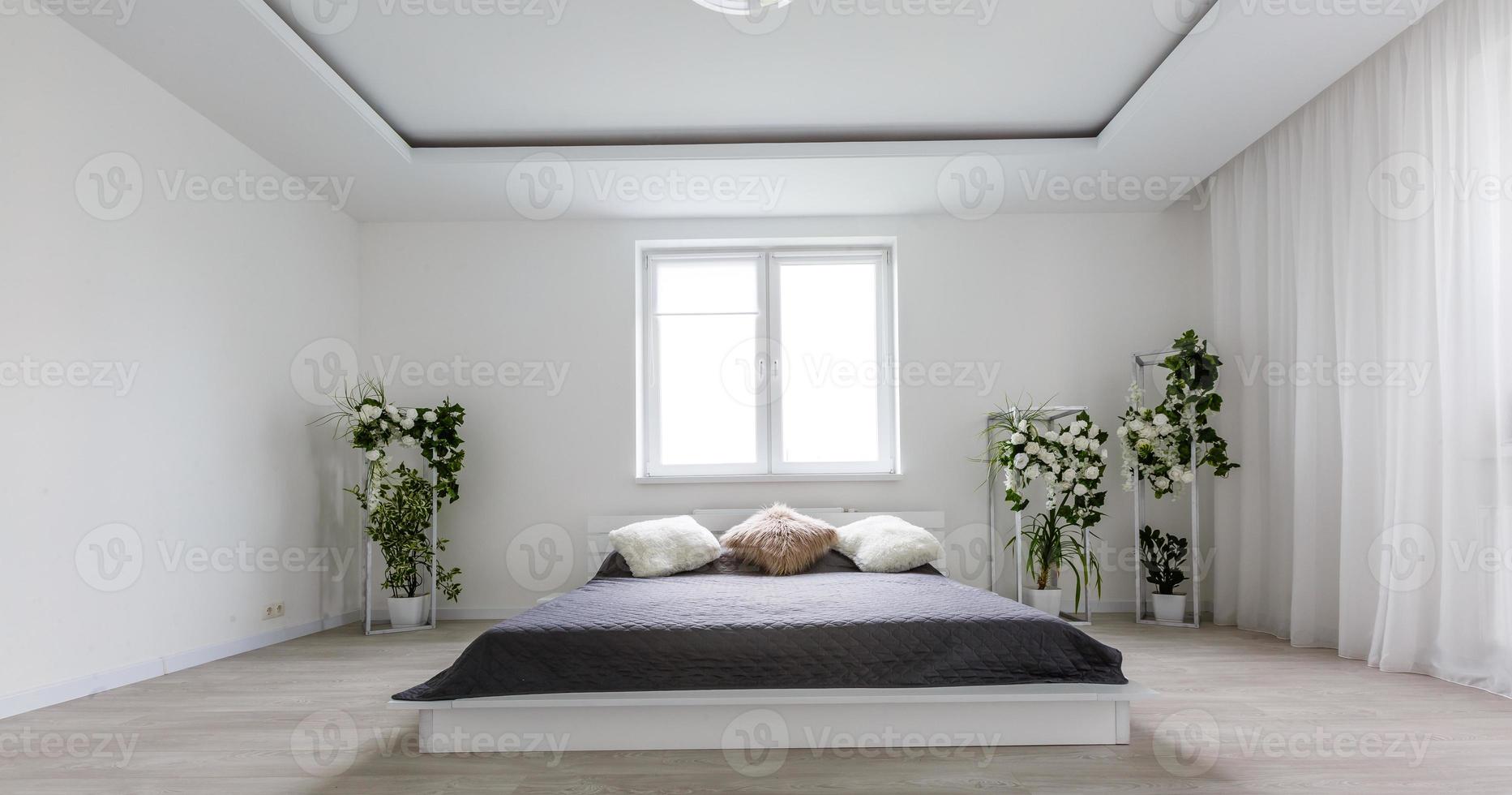 Light bedroom with white wall, large bed with grey bedding and handmade furniture photo