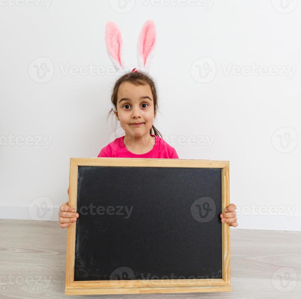 Very angry little girl wearing bunny ears sitting on a floor at home photo