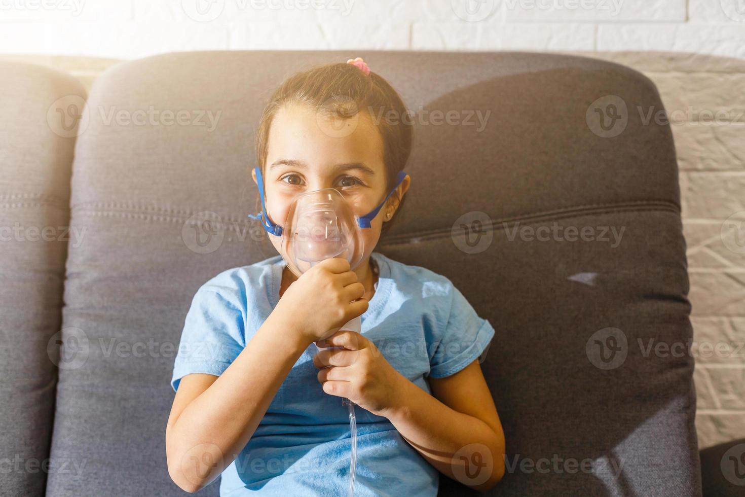 Little caucasian girl is breathing with special mask, which helps to stop asthma attack or relieve symptoms of respiratory disease. photo