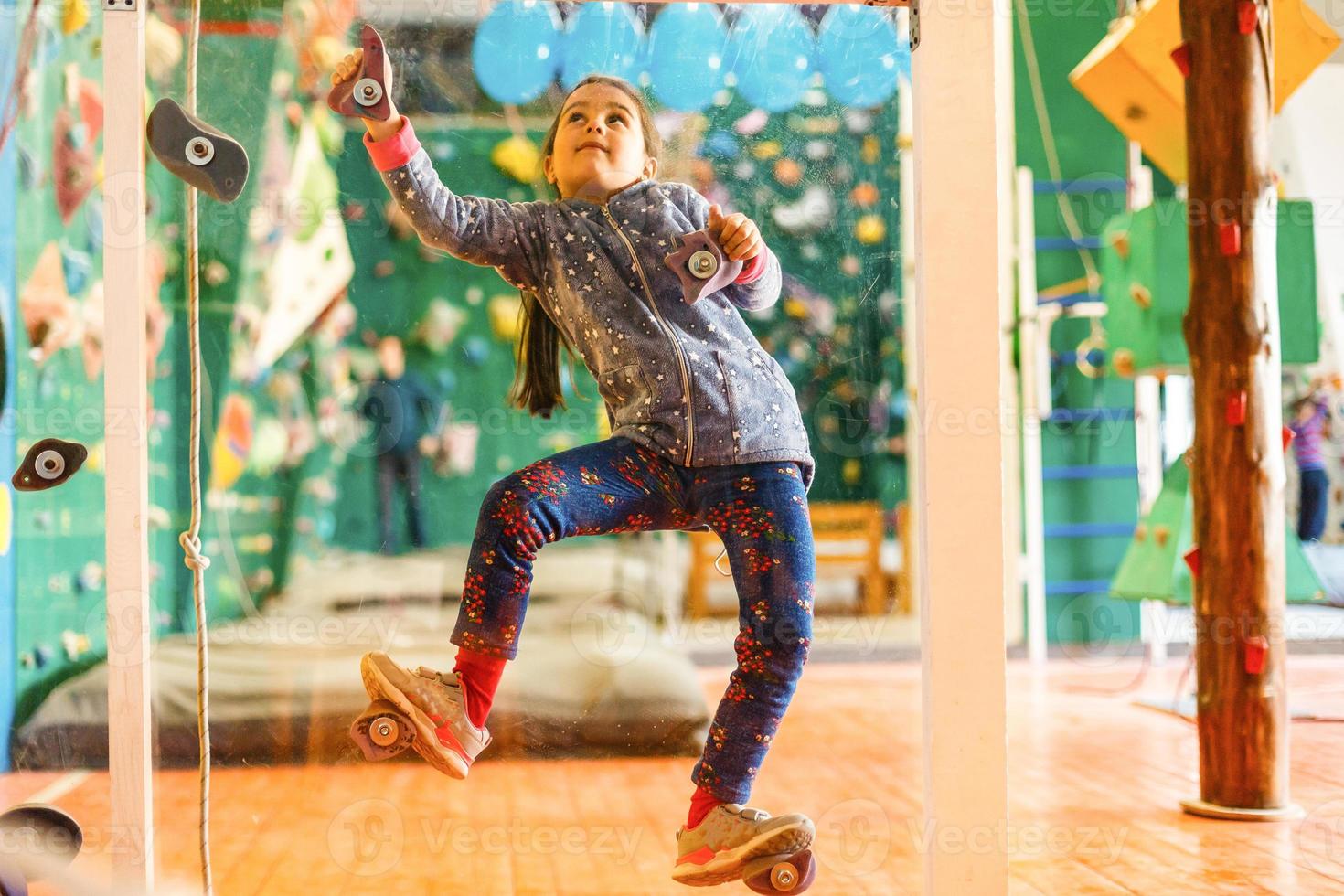 A young girl climbing a tall, indoor, man-made rock climbing wall photo