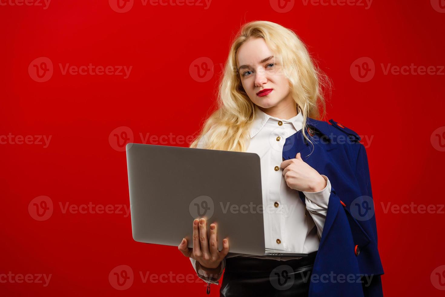 Beautiful young stylish female blogger and laptop - student or accountant posing on a red background. Advertising space photo