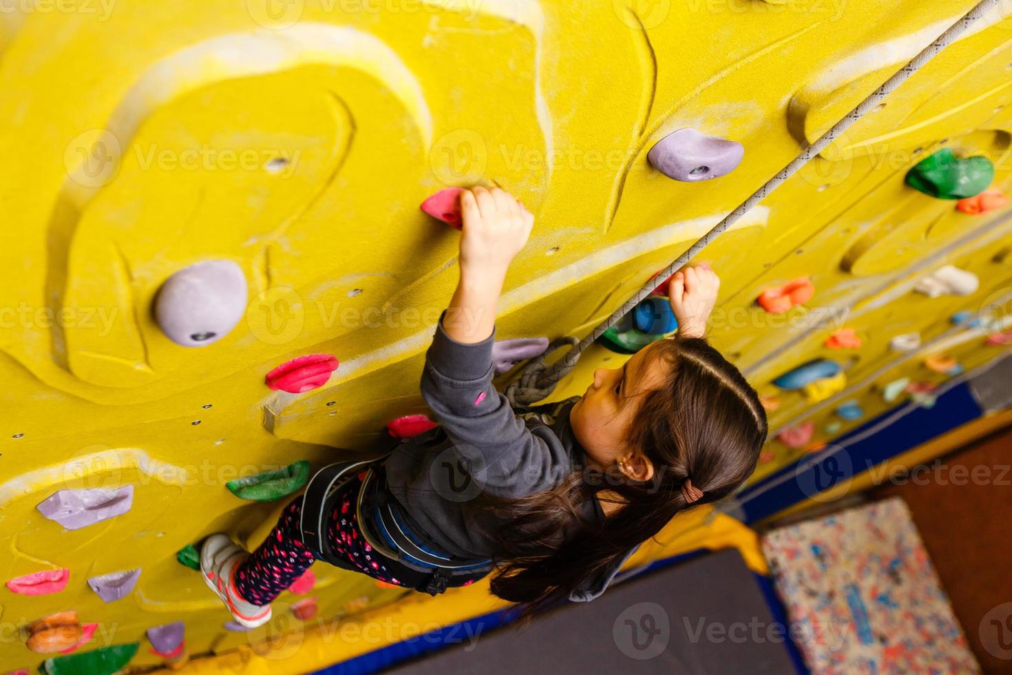little girl climbing a rock wall indoor. photo
