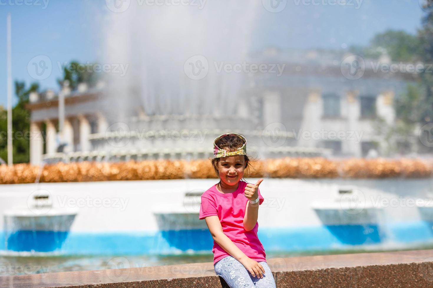 Loving life. Cheerful little girl having fun and posing near blue fountain water. Summer vacation. Happy child in summer hot day. photo