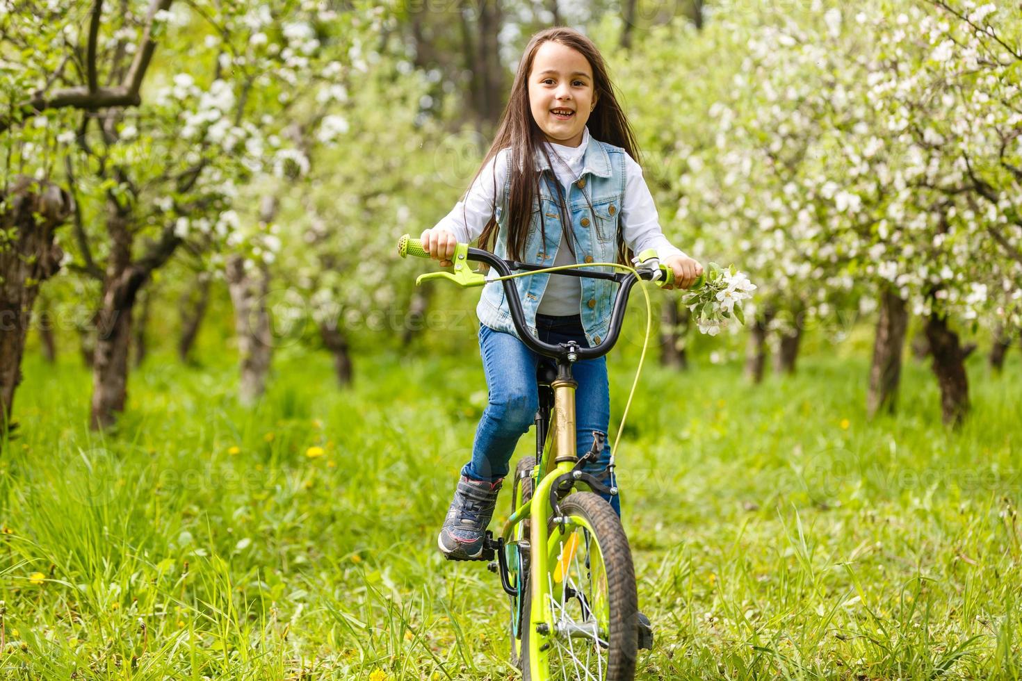 Child riding a bike on street with blooming cherry trees in the suburbs. Kid biking outdoors in urban park. Little girl on bicycle. Healthy preschool children summer activity. Kids play outside photo