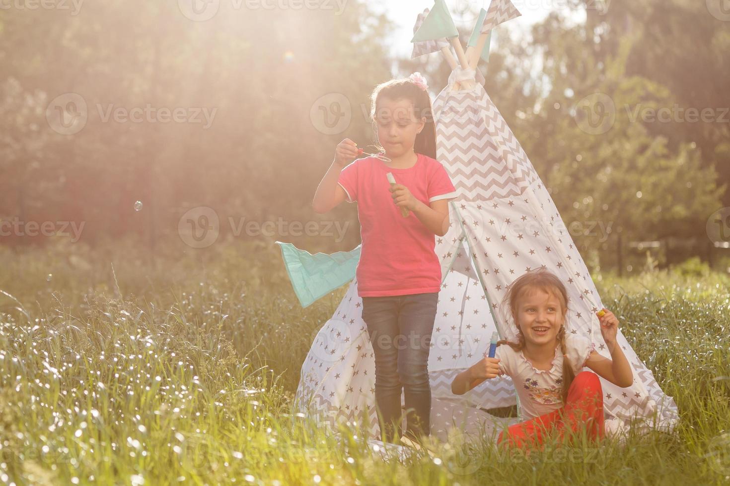 Two happy laughing little girls in camping tent in dandelion field photo
