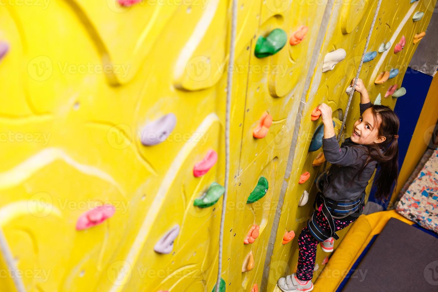 little girl climbing a rock wall indoor. photo