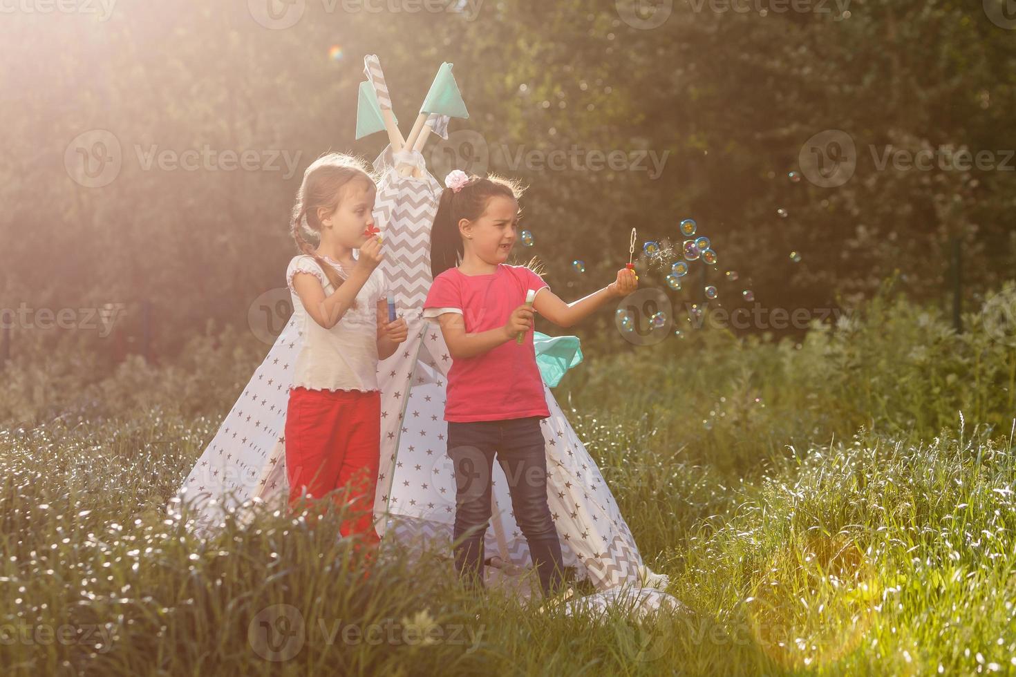 Two happy laughing little girls in camping tent in dandelion field photo