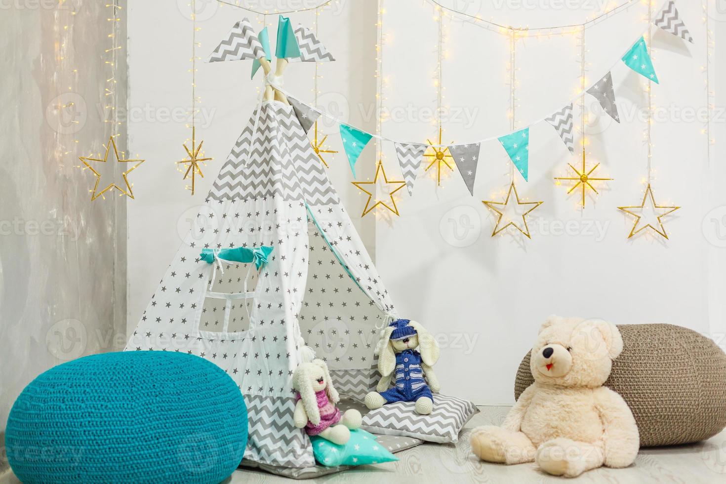 Teddy bear sits in a children's house wigwam on the background of an old wall photo