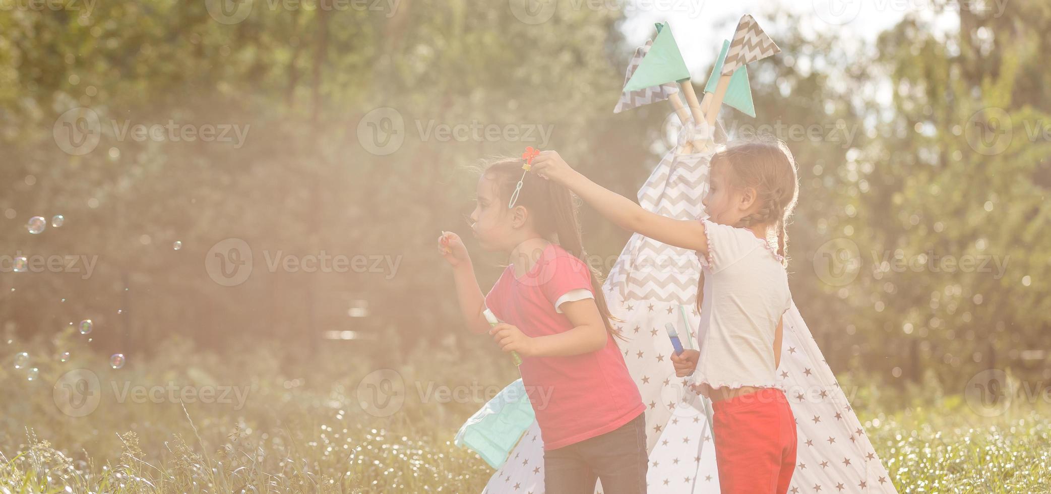 Two happy laughing little girls in camping tent in dandelion field photo