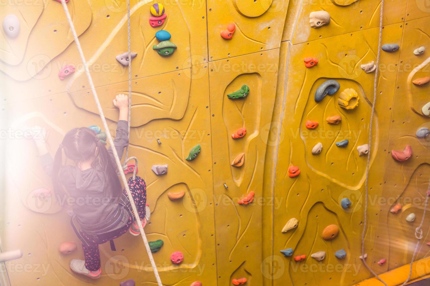 Little girl climbing a rock wall indoor photo
