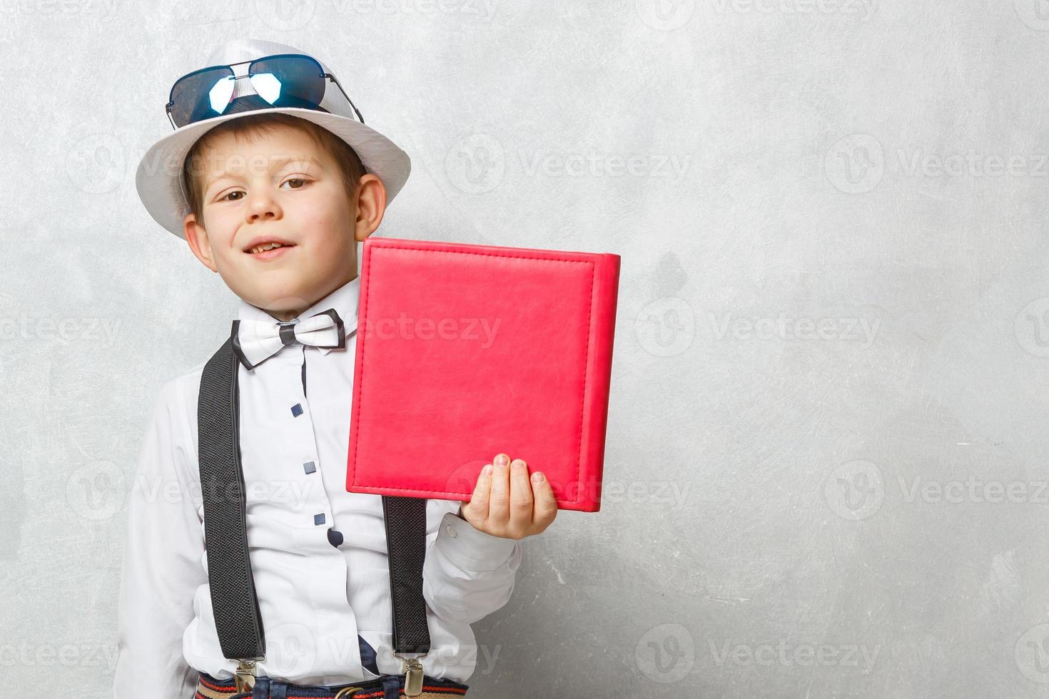 Back to school. Funny little boy in glasses pointing up on blackboard. Child from elementary school with book and bag. Education. Kid with a book photo