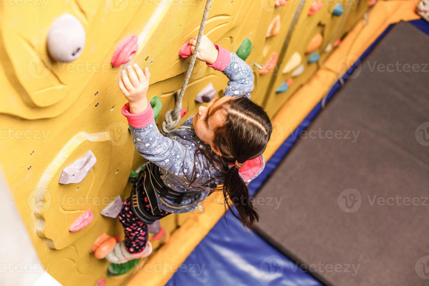Little girl climbing a rock wall indoor photo