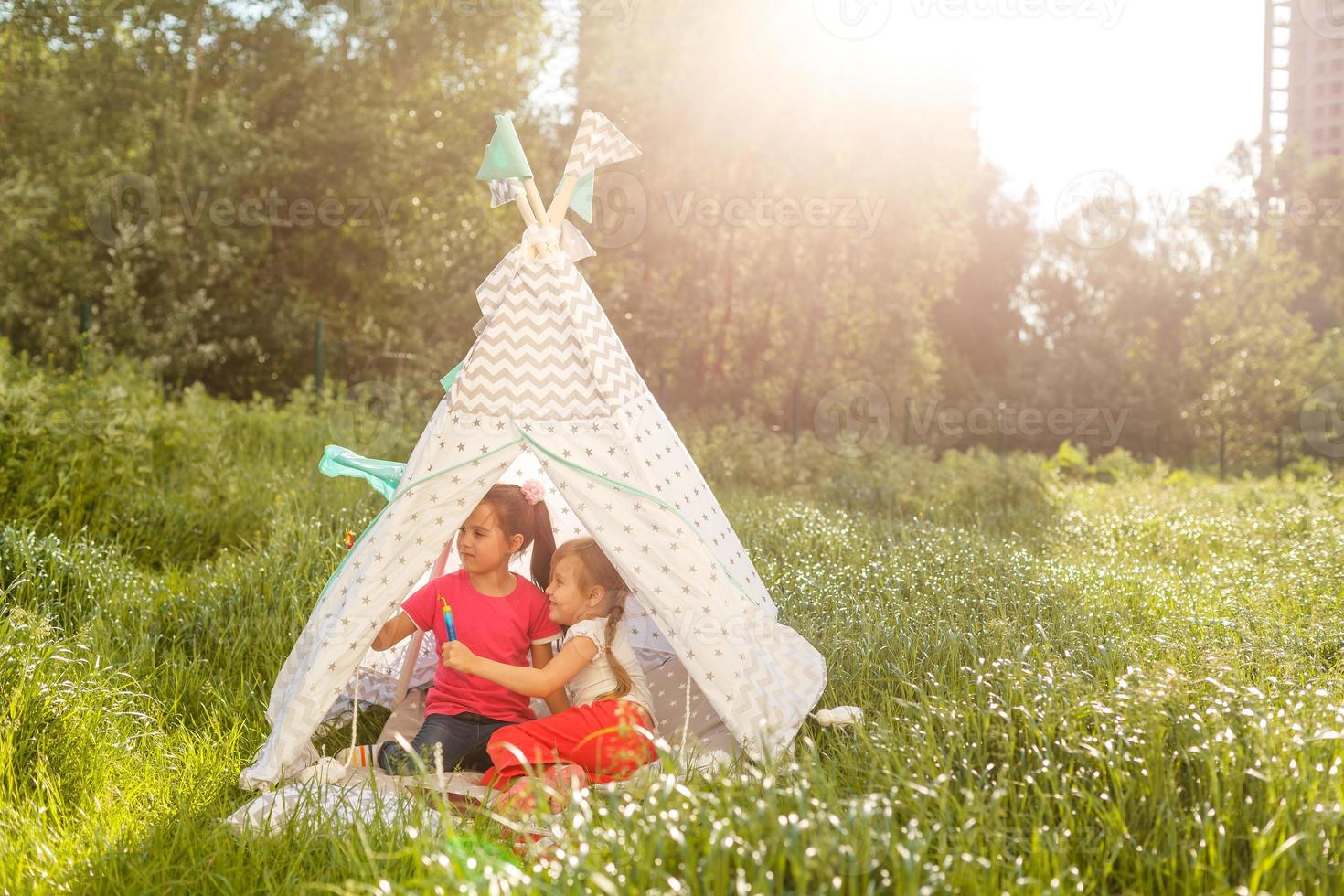 Two happy laughing little girls in camping tent in dandelion field photo