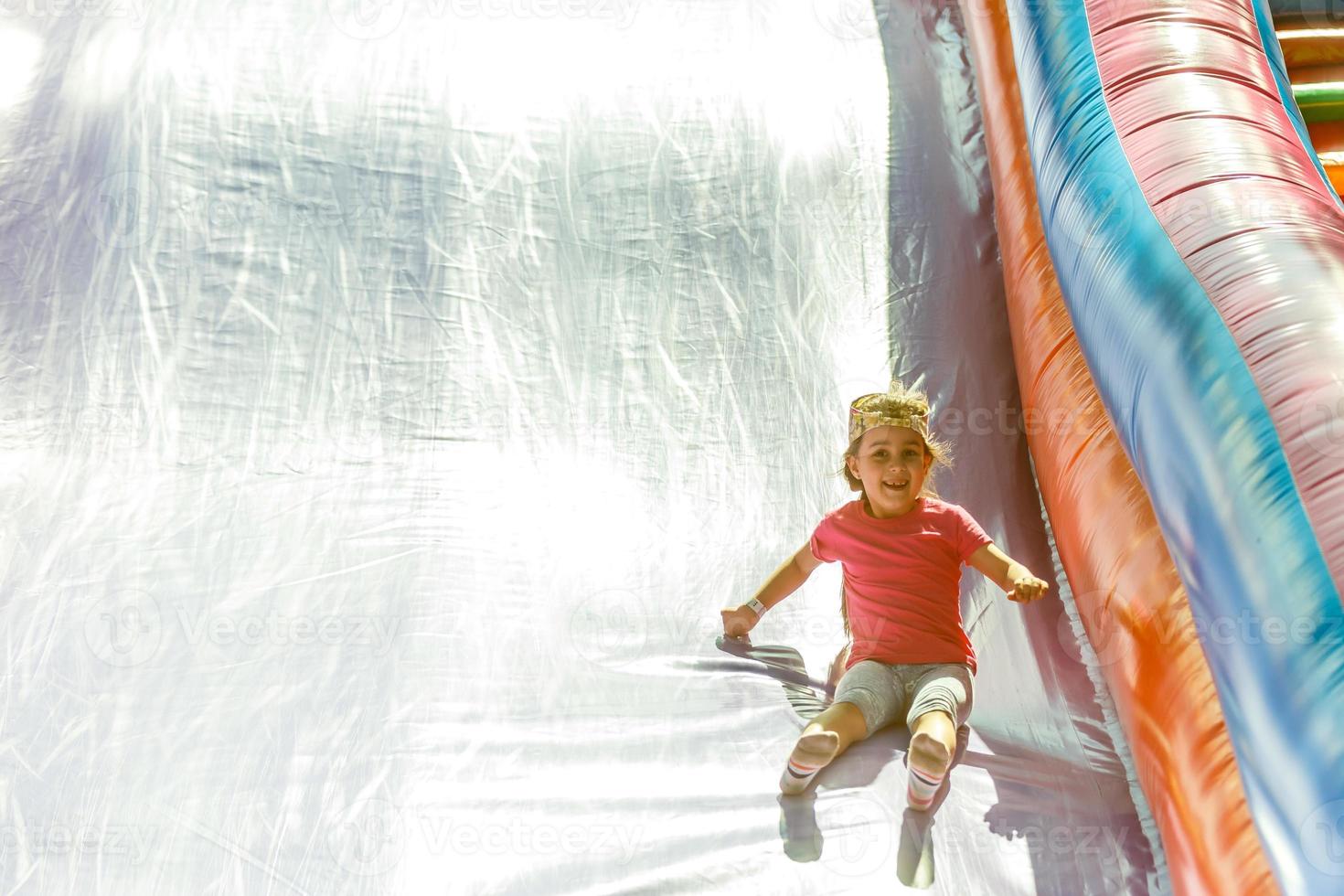 Happy little girl having lots of fun on a jumping castle during sliding. photo