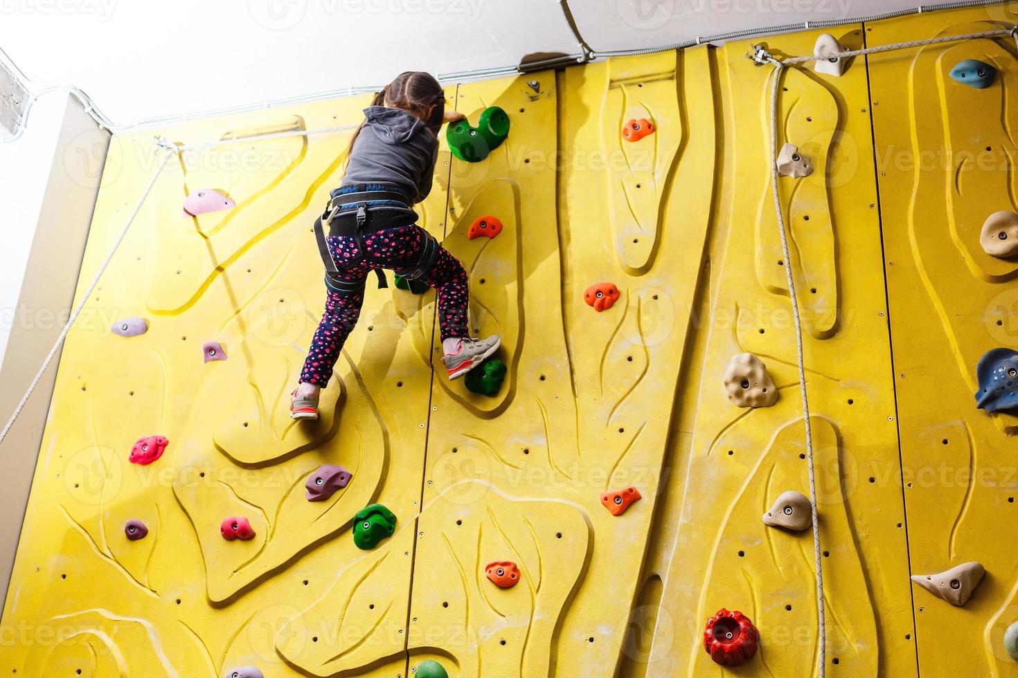 Little girl climbing a rock wall indoor photo