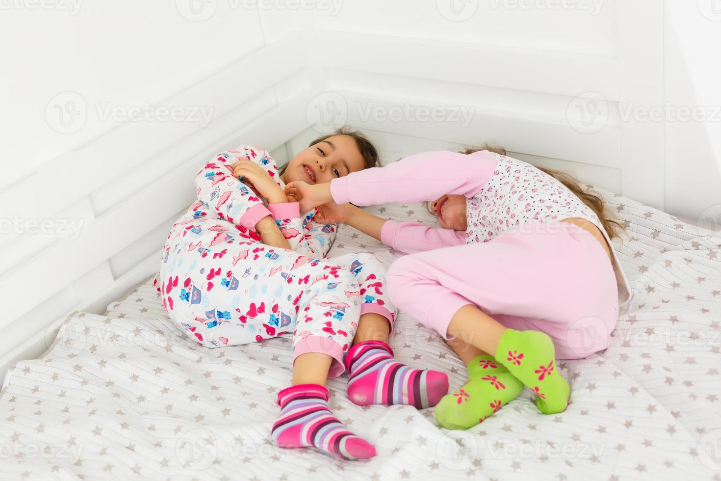 two little smiling lovely sisters in white bed, top, view photo