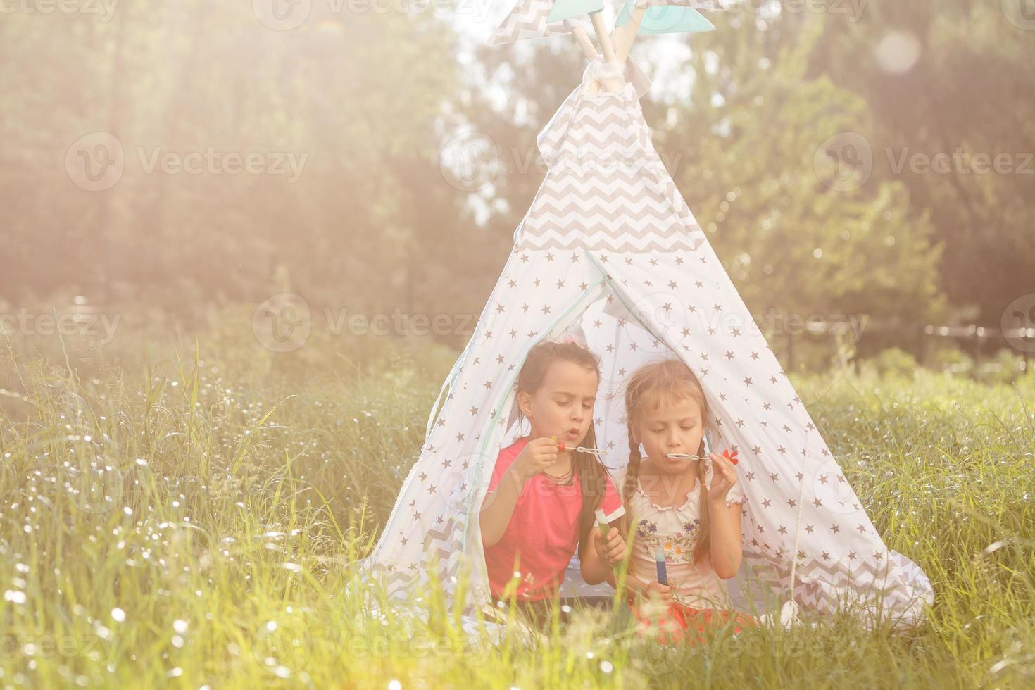 Two happy laughing little girls in camping tent in dandelion field photo