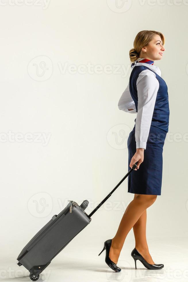 The stewardess goes and rolls her suitcase. White background. photo