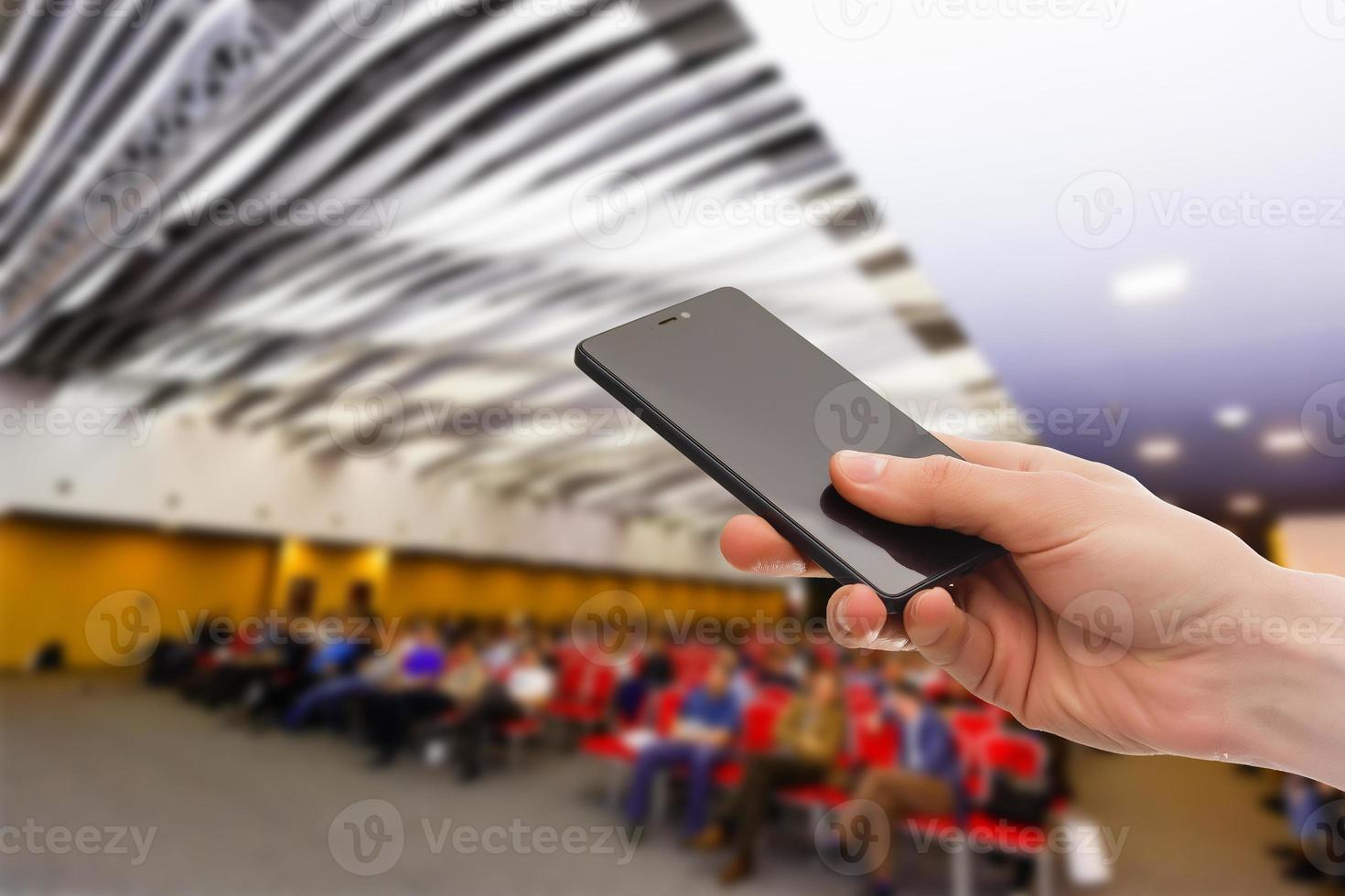 Man use mobile phone, blur image of people live in large conference room as background. photo