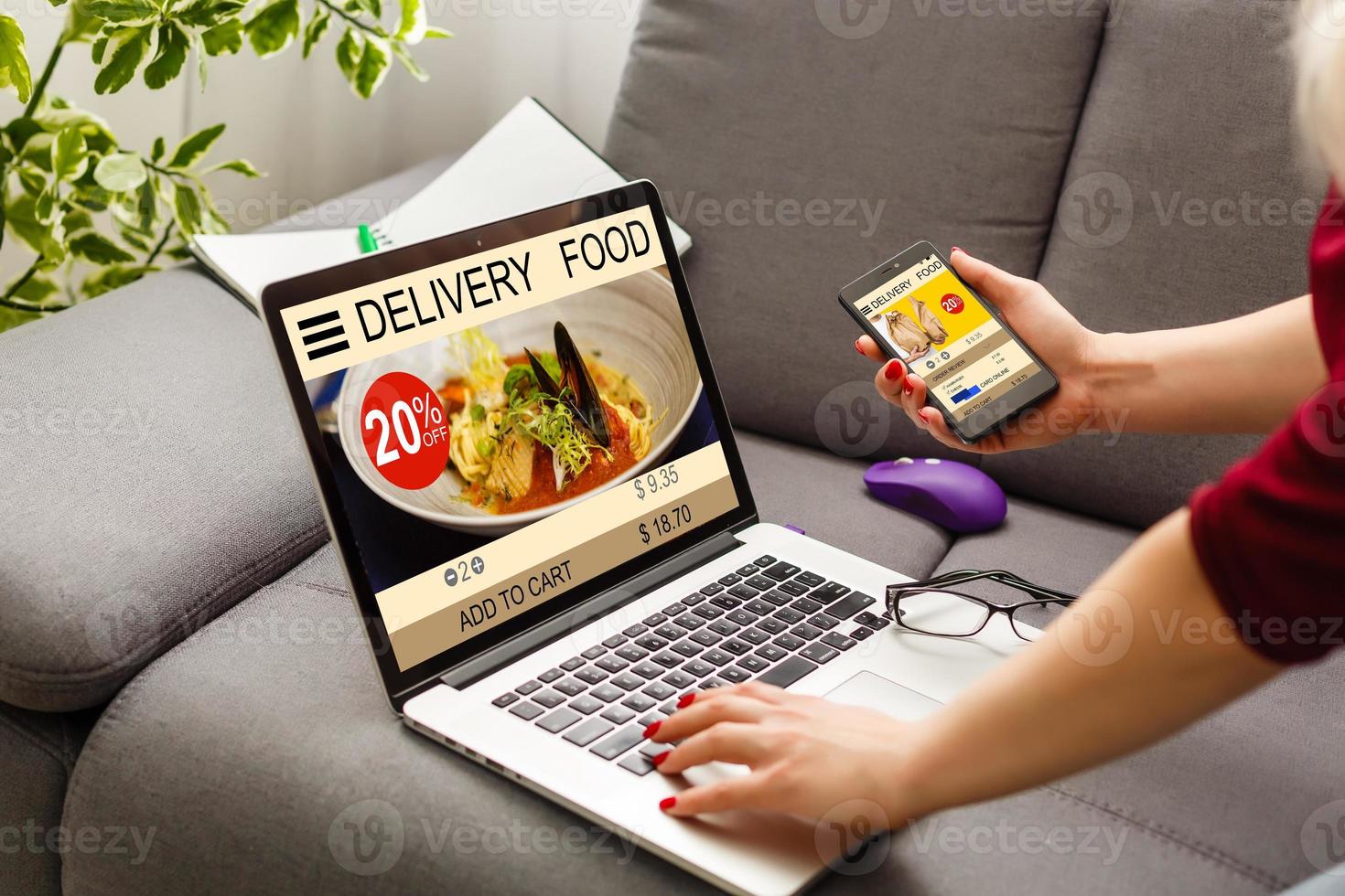 Woman using laptop and smartphone in cafe holding phone with app delivery food screen photo