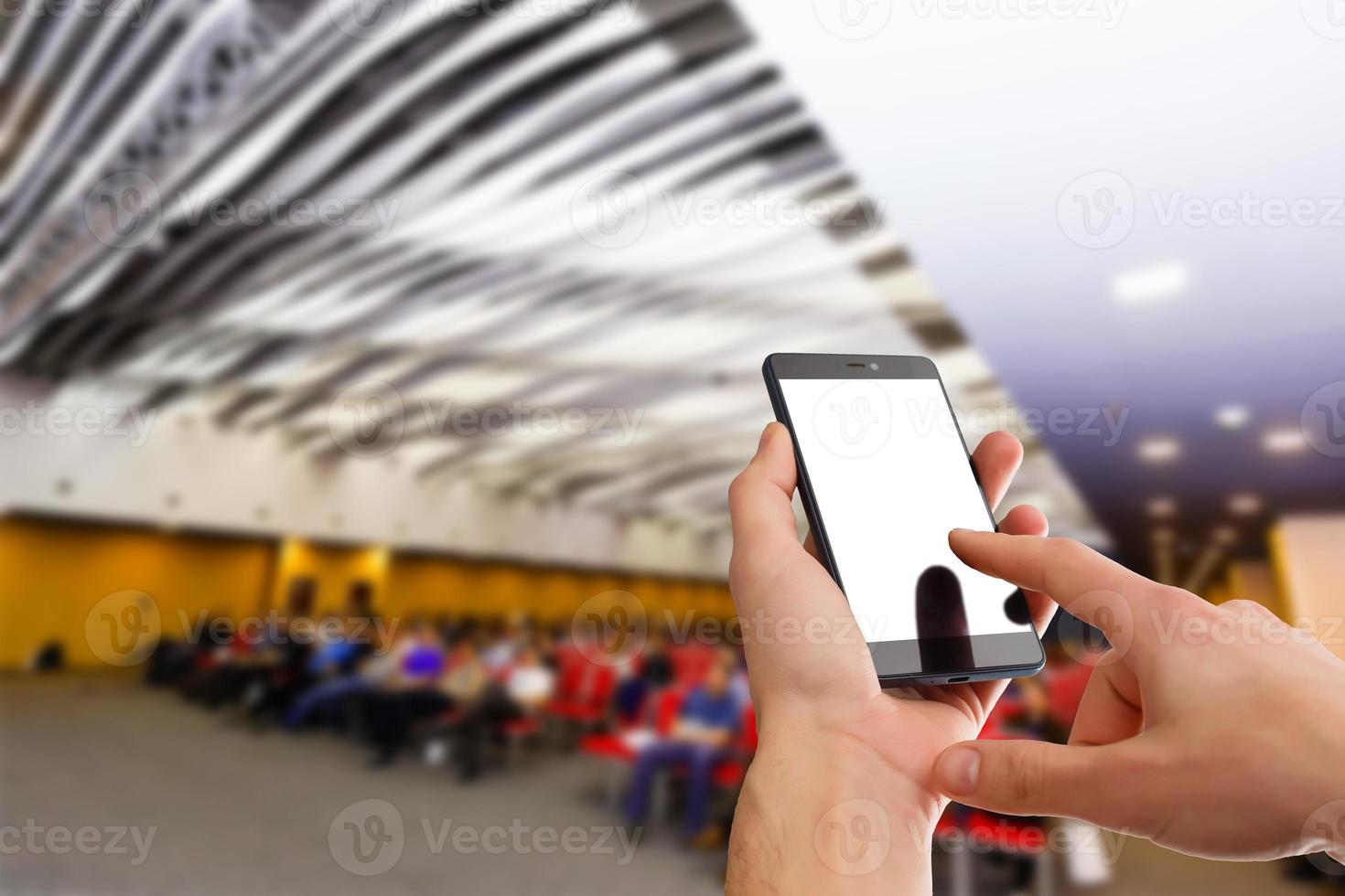 Man use mobile phone, blur image of people live in large conference room as background. photo