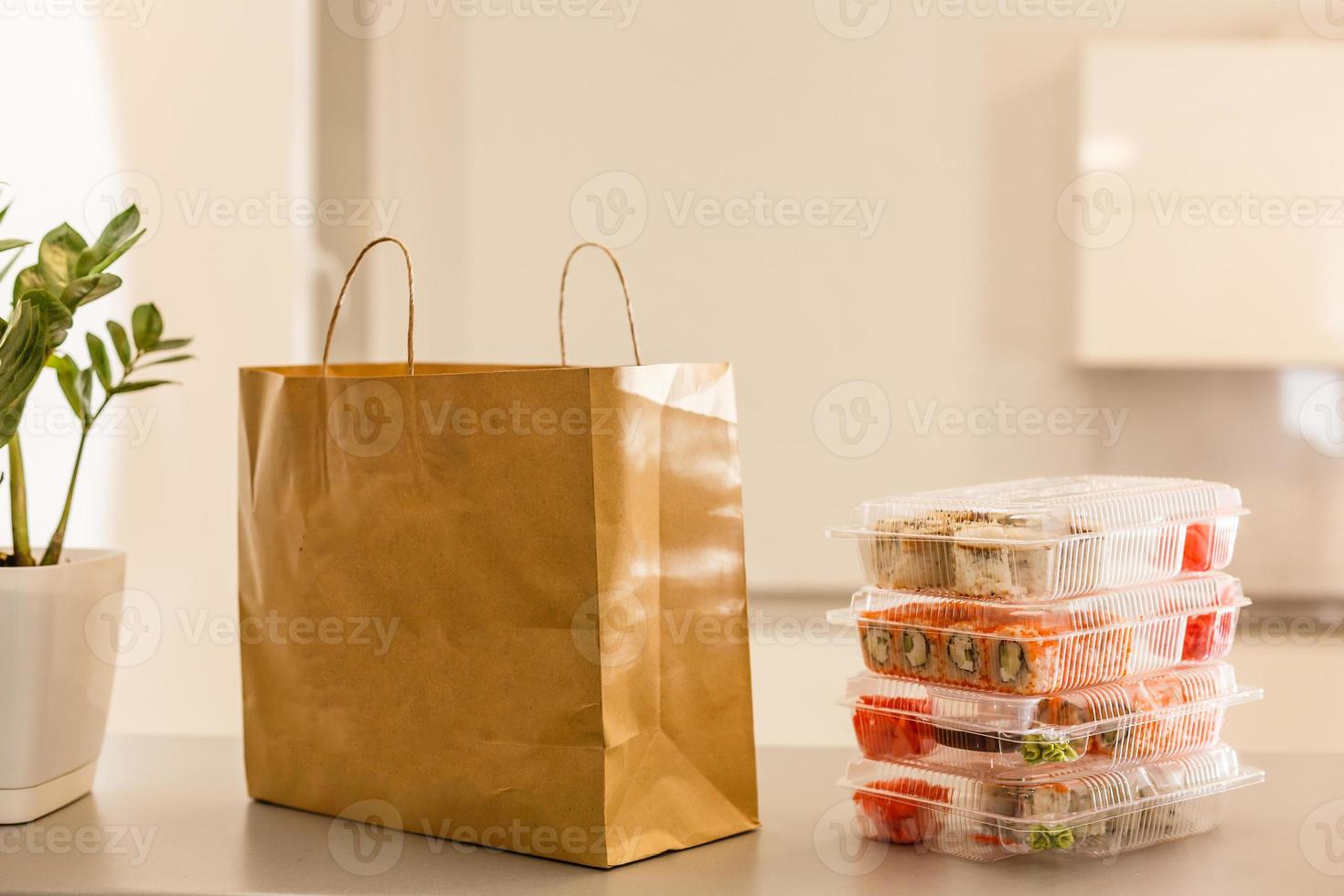 Sushi rolls in plastic box near paper package on white table. Delivery. Take away. photo