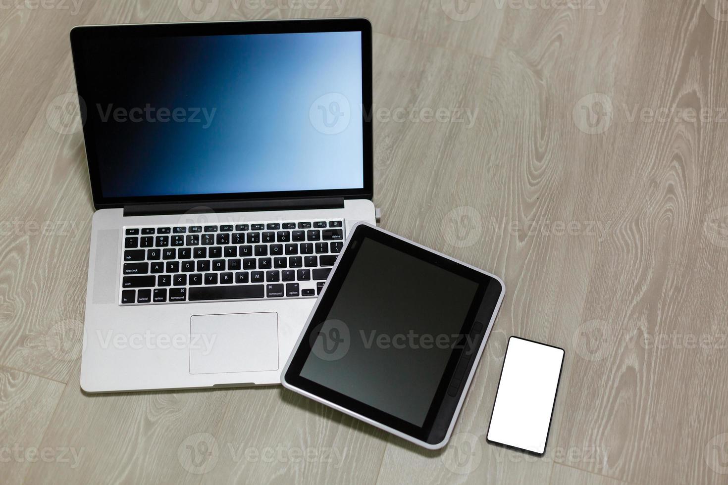 Modern laptop, mobile phone, tablet, and notebook on white wooden background photo