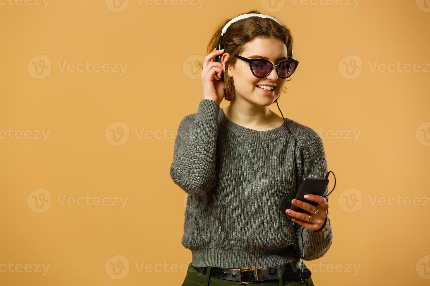 Smiling woman listening music in headphones and using smartphone over yellow background photo