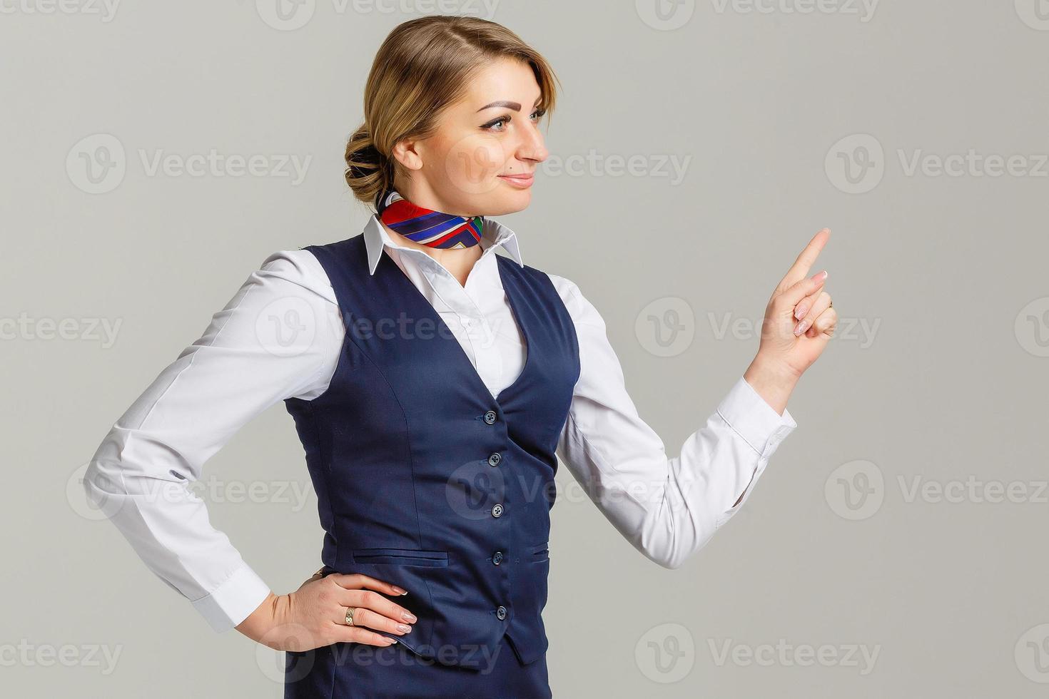 encantadora azafata vestida con uniforme azul señalando con el dedo el fondo gris foto