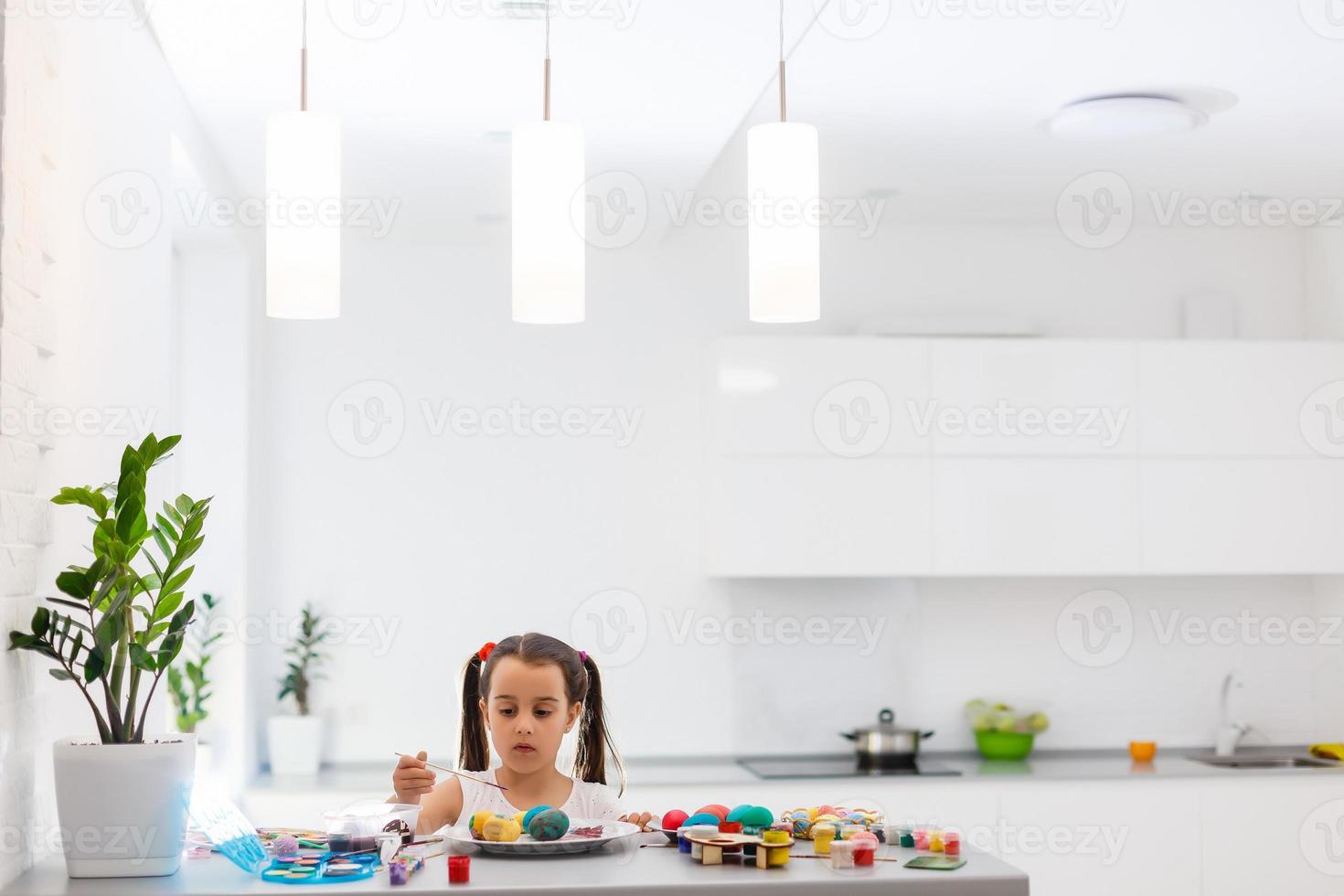 Little girl painting Easter eggs in the kitchen photo