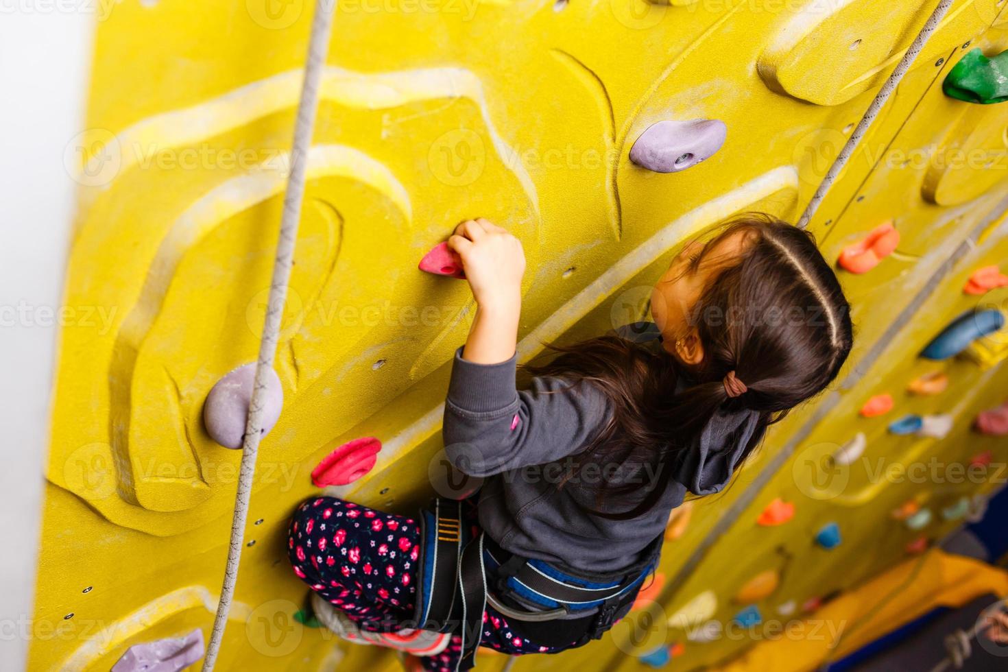 little girl climbing a rock wall indoor. photo