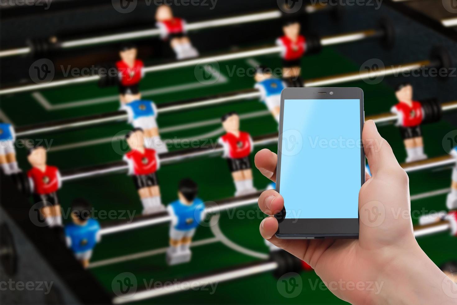 A male hand holding a mobile phone which displays a match on the touch screen. The big green screen is in contrast with the overexposed background. An image on an interior background. photo