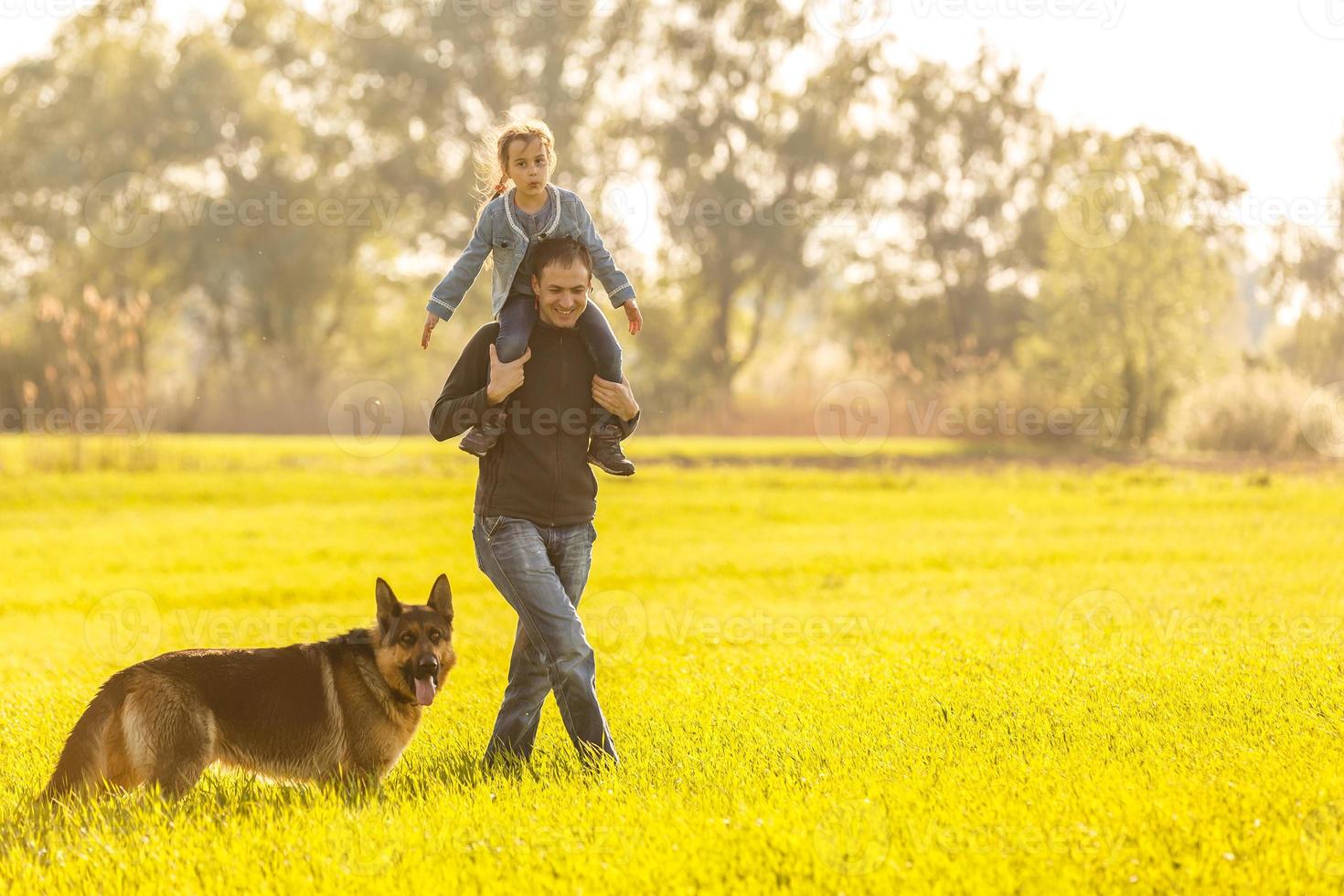 Happy family with dog walking. Little girl sitting on dad's shoulder photo