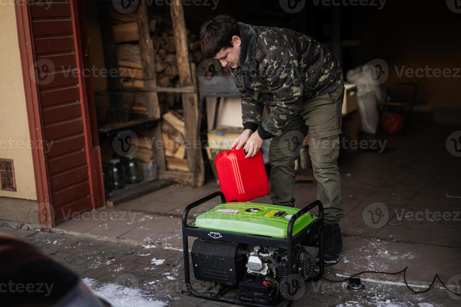 Man wear in military jacket pour gasoline from canister in portable mobile backup standby generator. photo