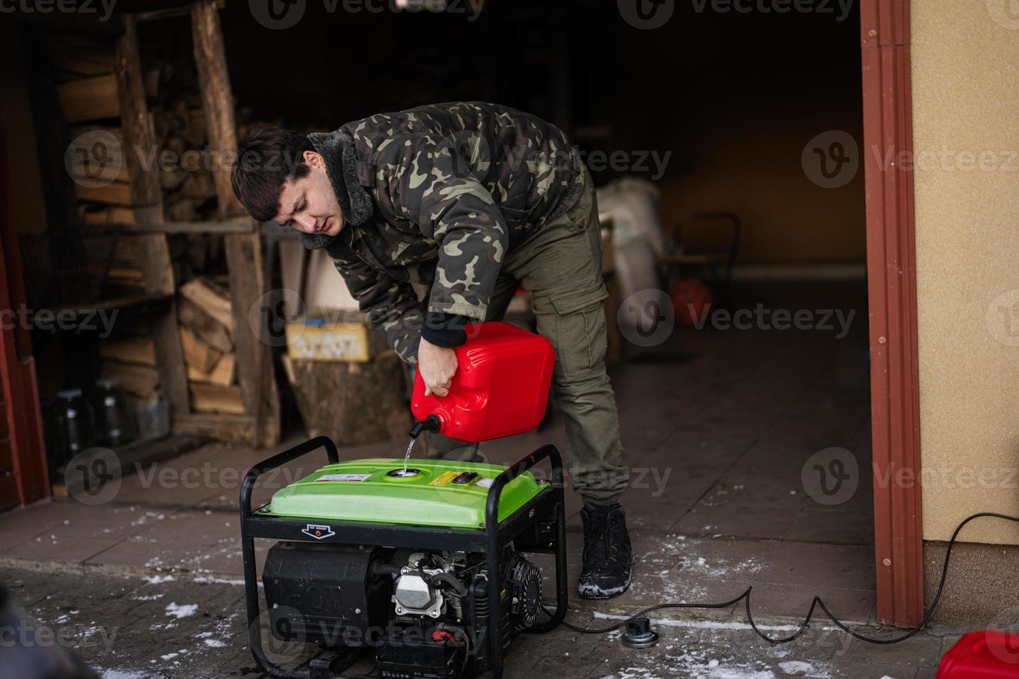 Man wear in military jacket pour gasoline from canister in portable mobile backup standby generator. photo