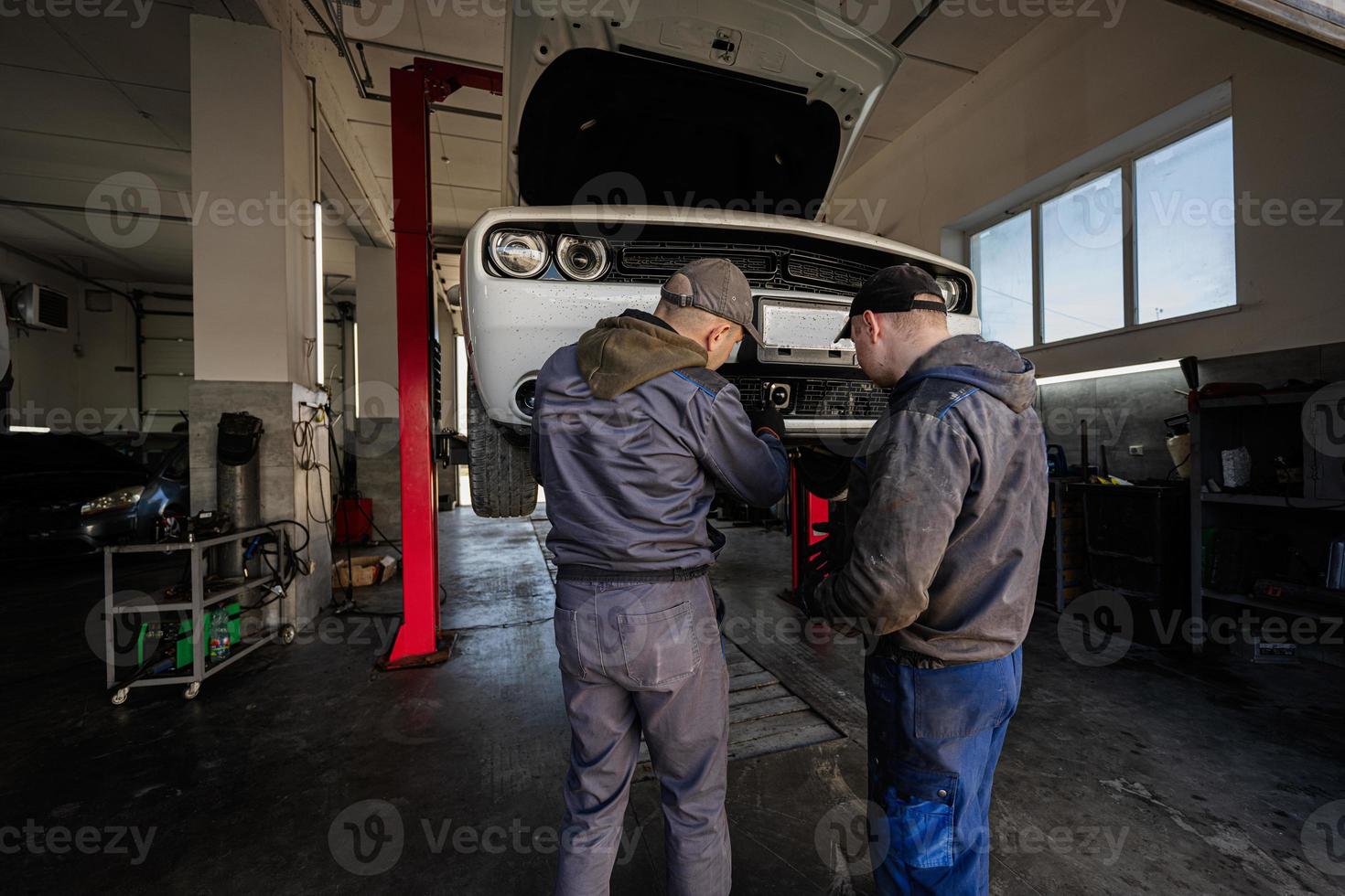 Two mechanic in service repair station calibrate the distronic in muscle car in lift. photo