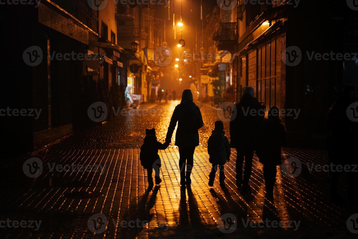 Back of silhouettes family walking in night city. photo