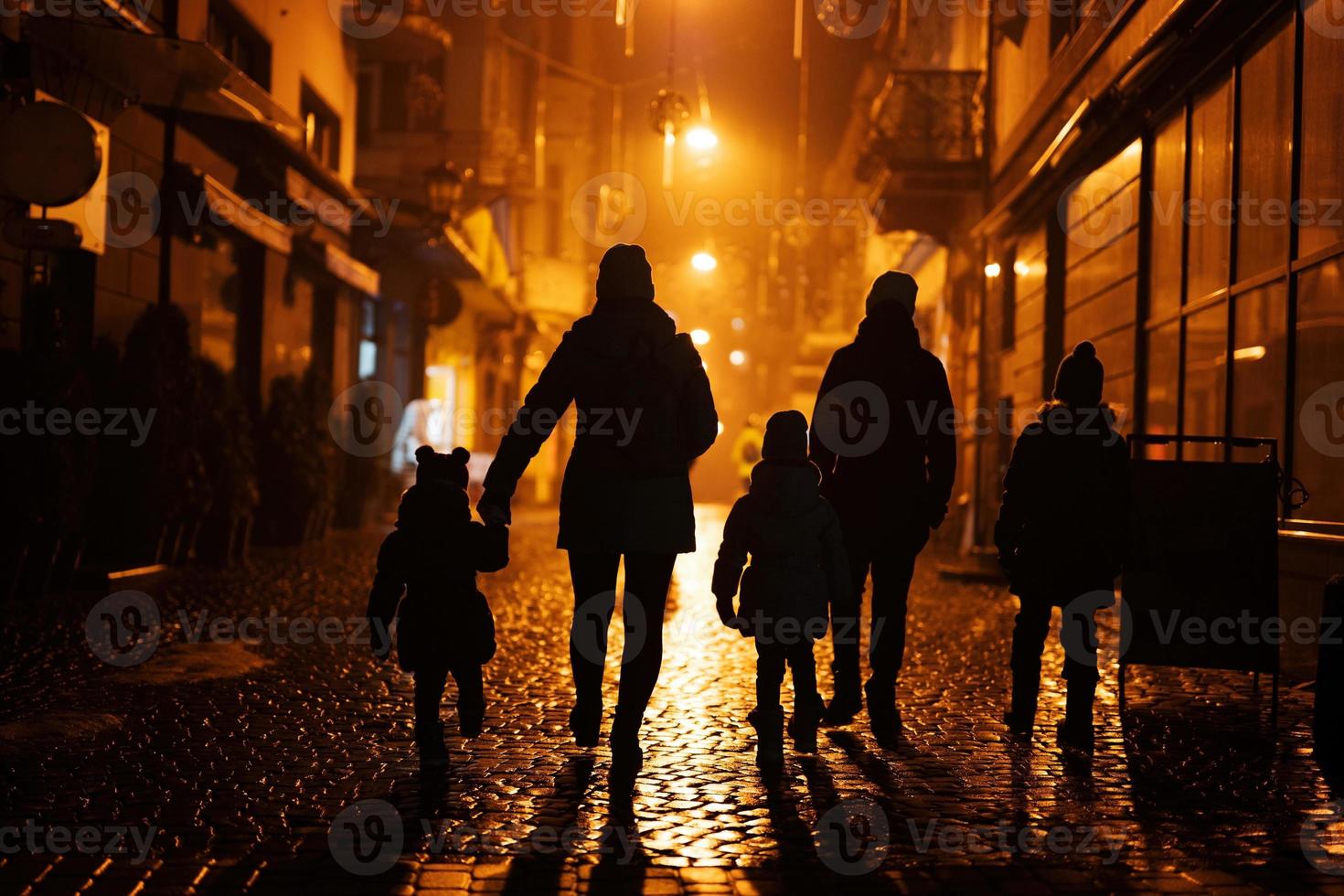 Back of silhouettes family walking in night city. photo